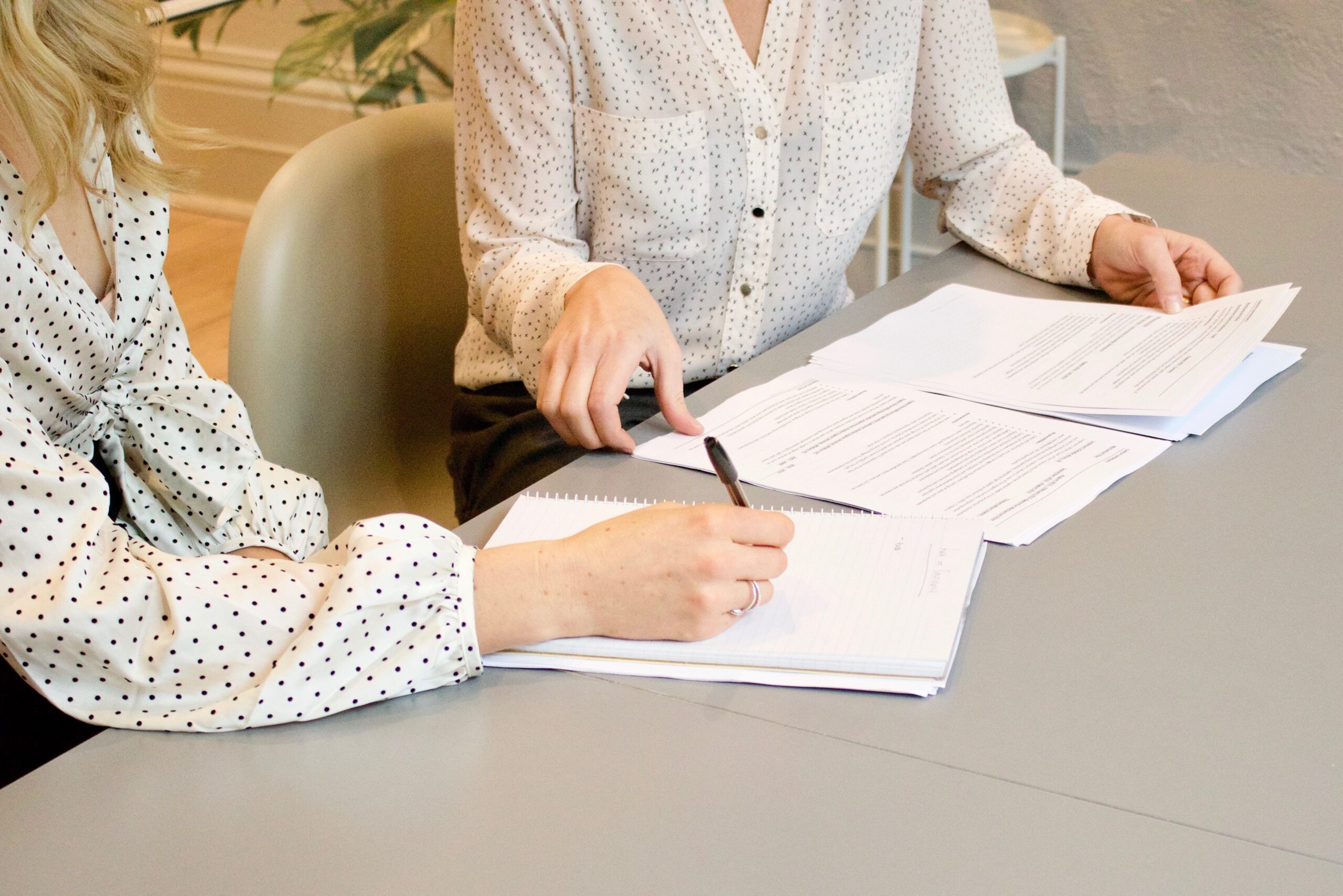 woman signing on white printer paper beside woman about to touch the documents